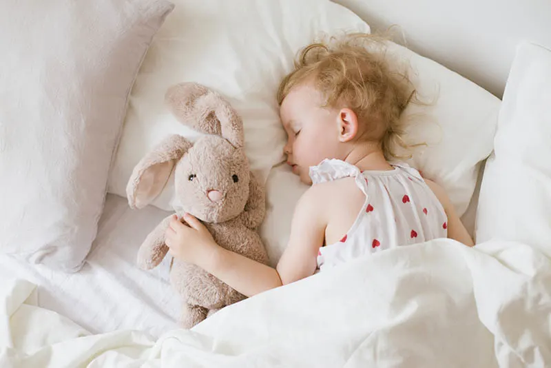 niedlichen kleinen Mädchen schlafen mit Hase Spielzeug im Bett