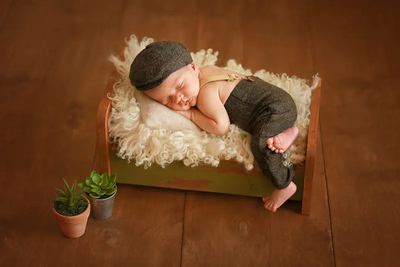 niedlichen neugeborenen Baby in modischen Anzug schlafen in einem Kinderbett für Fotoshooting