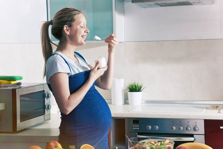 schwangere Frau steht in der Küche und isst cremigen Käse