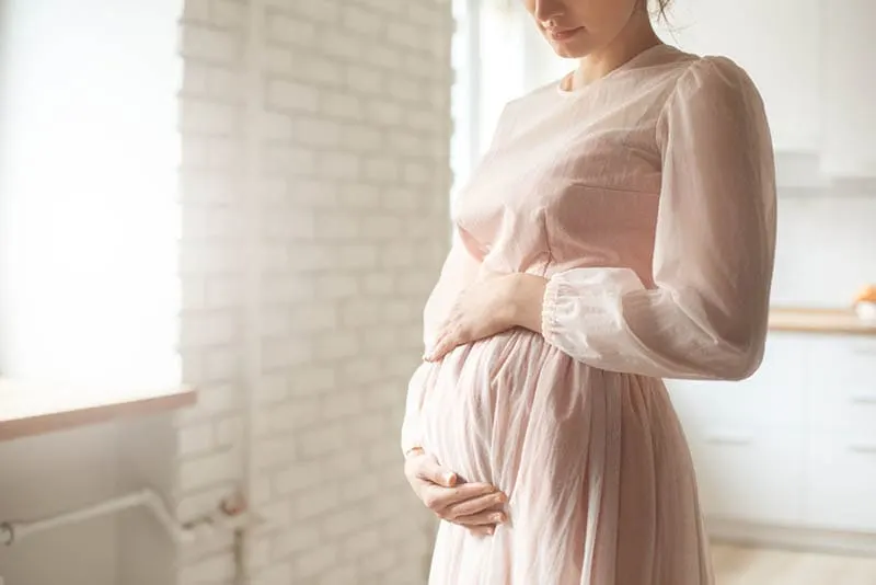 schöne junge schwangere Frau trägt hübsche Mutterschaft Kleid und hält ihren Bauch