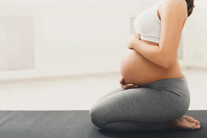 schwangere Frau, die Yoga praktiziert und ihren Bauch streichelt