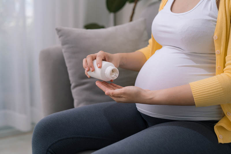 schwangere Frau, die auf der Couch sitzt und Pillen von der weißen Flasche nimmt