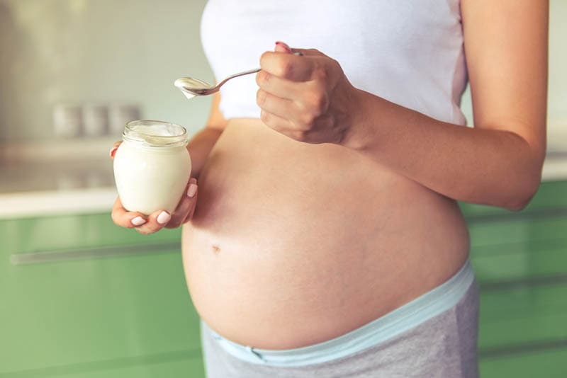 schwangere Frau hält ein Glas mit cremigem Käse und den Löffel in der Küche