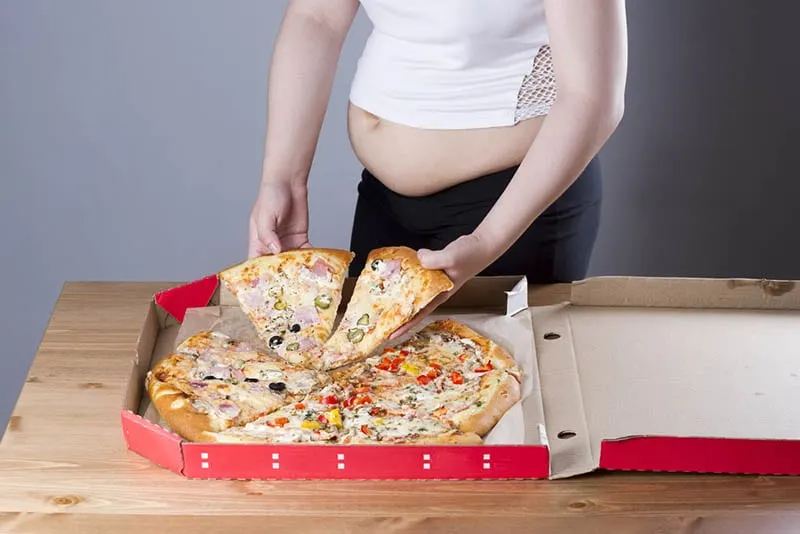 schwangere Frau schnappt sich ein Stück Pizza vom Pizzaboten auf dem Tisch