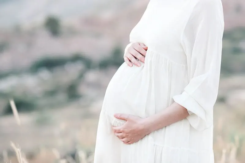 schwangere Frau trägt weißes Umstandskleid und steht im Feld