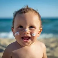 süßer kleiner Junge mit Sonnencreme auf Gesicht, das am Strand steht