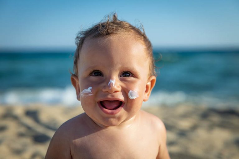 süßer kleiner Junge mit Sonnencreme auf Gesicht, das am Strand steht