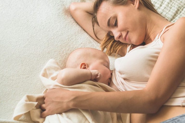 hübsche Mutter, die ihr Baby auf dem Bett stillt und lächelt