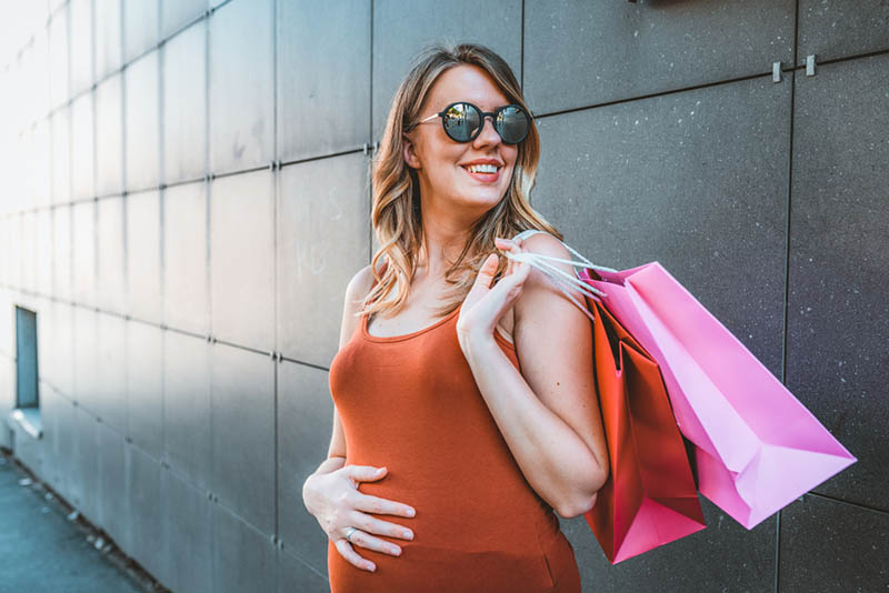stilvolle schwangere Frau mit Sonnenbrille hält Einkaufstaschen im Freien