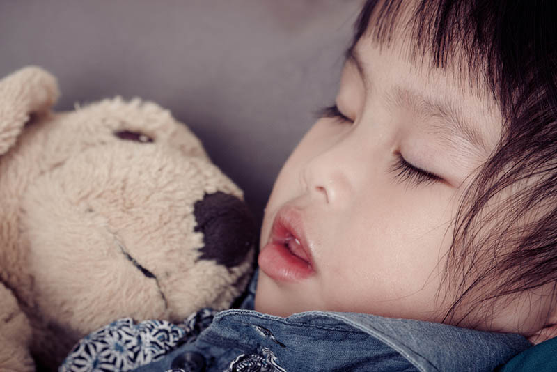 süßes Baby Mädchen schlafen mit offenem Mund und ein Spielzeug in der Umarmung