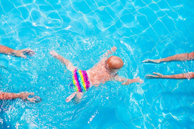 süßes Baby, das im Pool von einem Elternteil zum anderen schwimmt