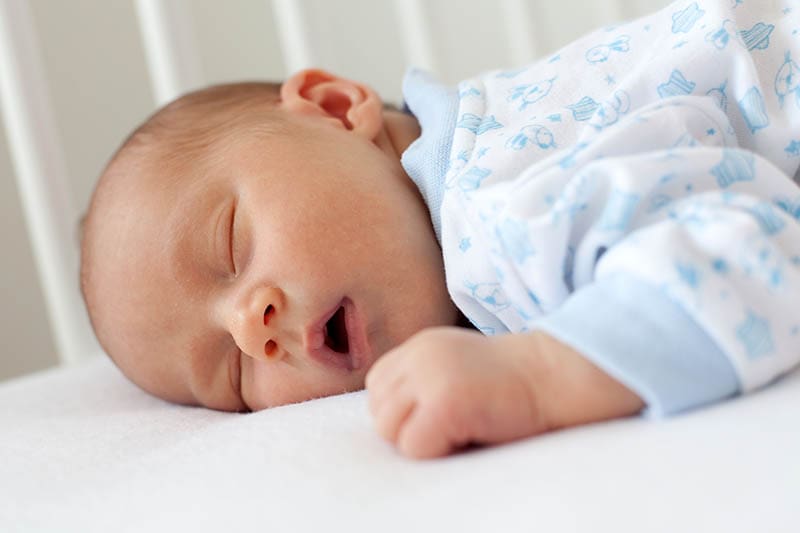 süßes Baby im Pyjama, das mit offenem Mund in der Krippe schläft