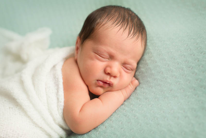 süßes Baby mit weißer Decke bedeckt schlafen auf dem Bauch