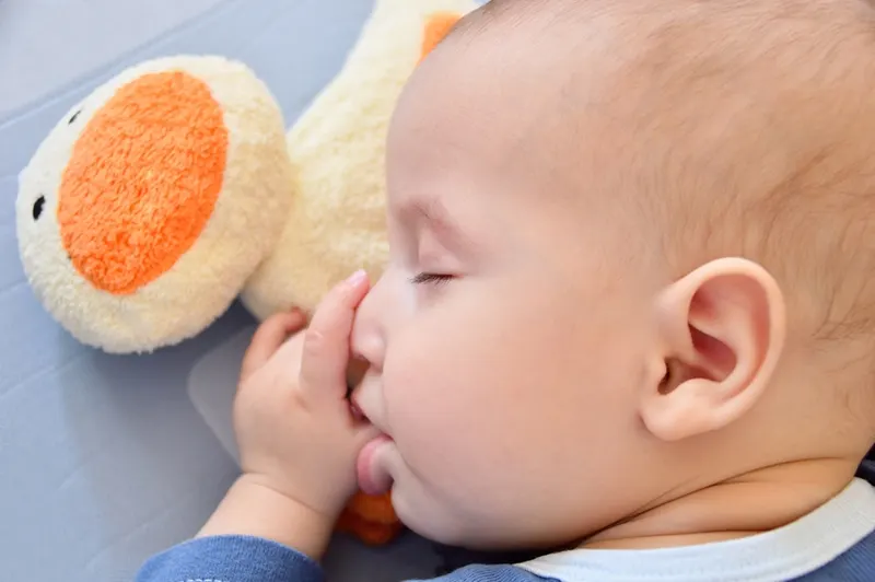 süßes Baby saugt seinen Daumen im Schlaf mit Spielzeug neben ihm