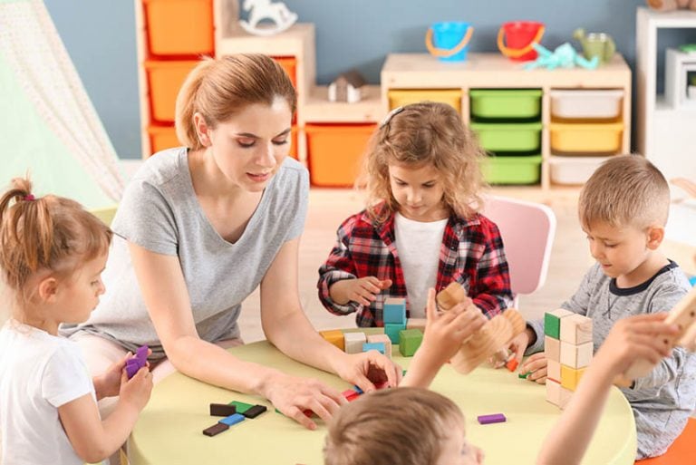 Lehrerin spielt mit Kindern mit Würfeln am Tisch