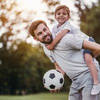 glücklicher Vater, der seinen Sohn mit Fußball auf dem Rücken trägt