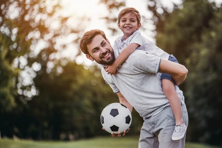 glücklicher Vater, der seinen Sohn mit Fußball auf dem Rücken trägt