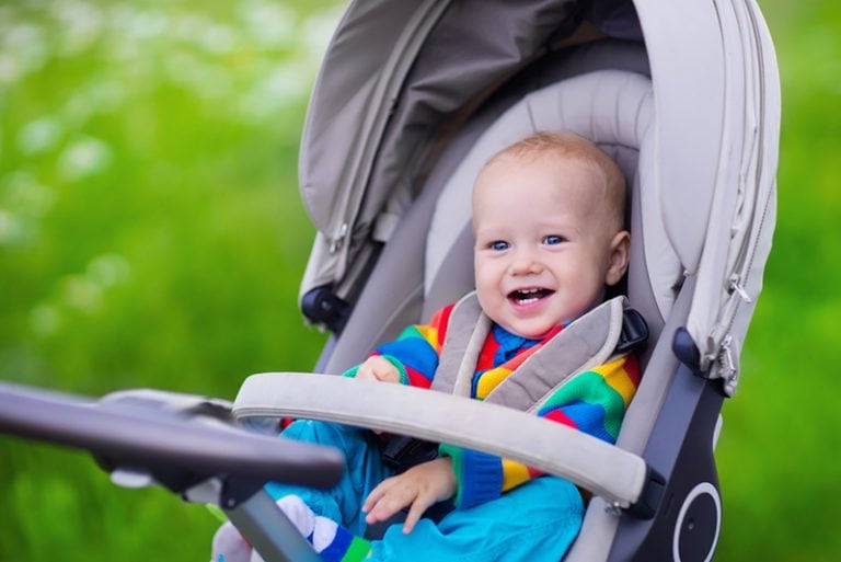 entzückender kleiner Junge, der in einem Kinderwagen sitzt und lächelt