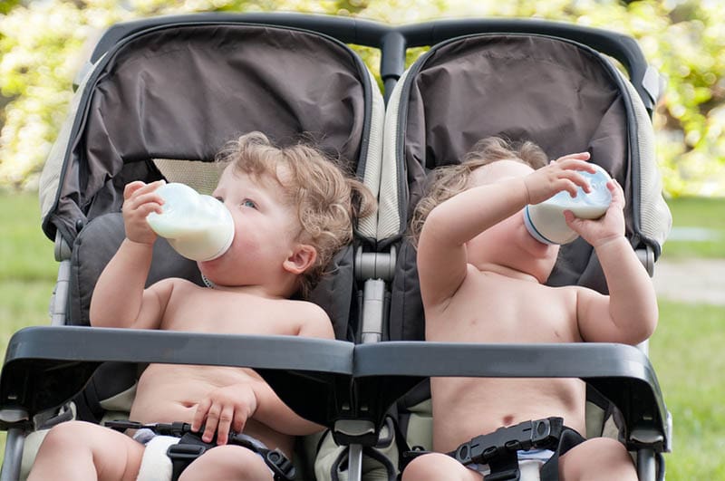 zwei Babys trinken Milchflaschen in den Zwillingskinderwagen im Freien