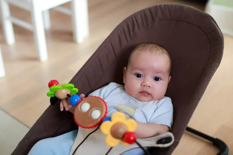 Baby-Junge in einer Babywippe mit hängenden Spielzeug über