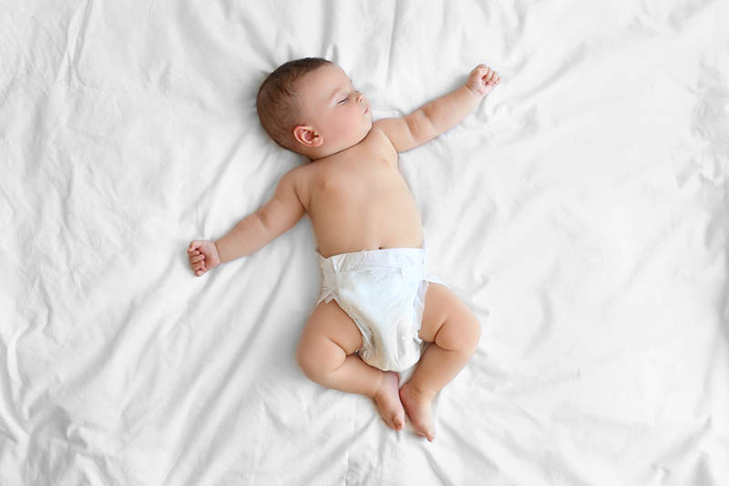 Baby Junge trägt Windeln schlafen auf großen Bett in weißem Laken
