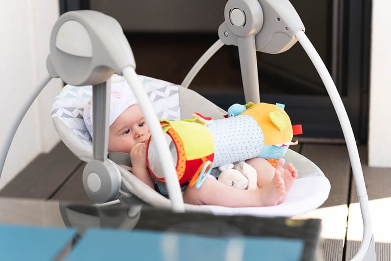 Baby liegend in einer elektrischen Schaukel mit einem Spielzeug