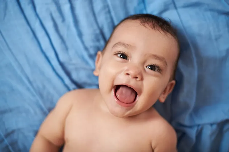 Baby mit offenem Mund auf Bett blaue Decke legen