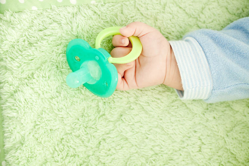 Baby's kleine Hand hält grünen Schnuller auf dem Bett