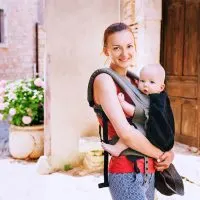 lächelnde junge Mutter, die ihr Baby in einer Trage im Freien trägt