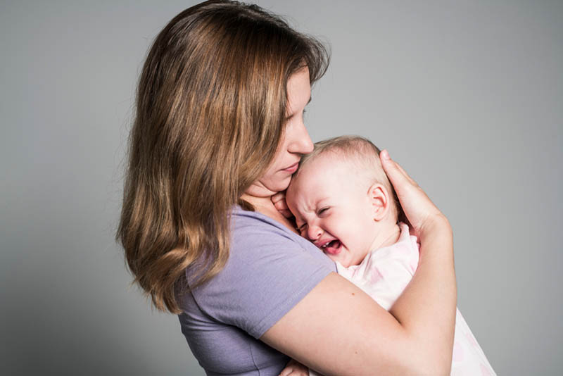 Besorgte Mutter umarmt und streichelt weinendes Baby in den Armen