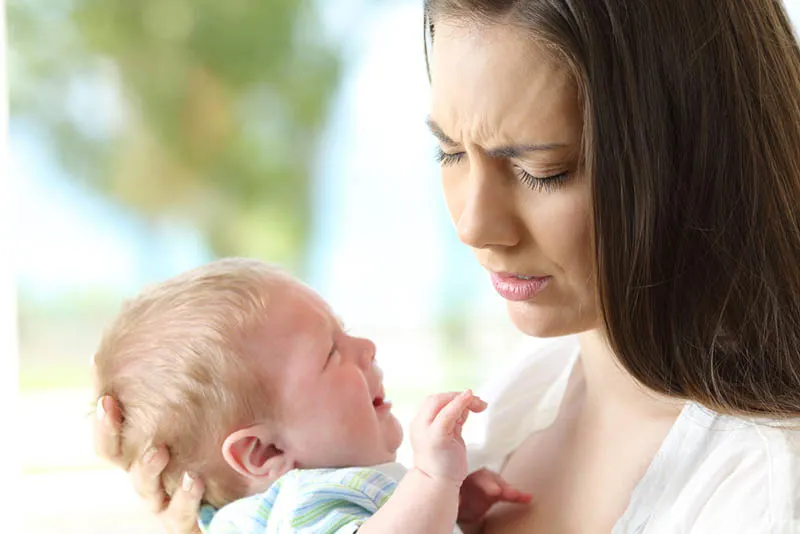 Besorgte junge Mutter hält ihr weinendes Baby im Arm