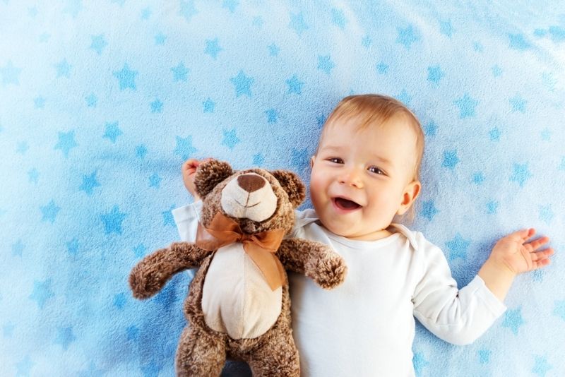 Einjähriges Baby, das mit einem Plüsch-Teddybär im Bett liegt