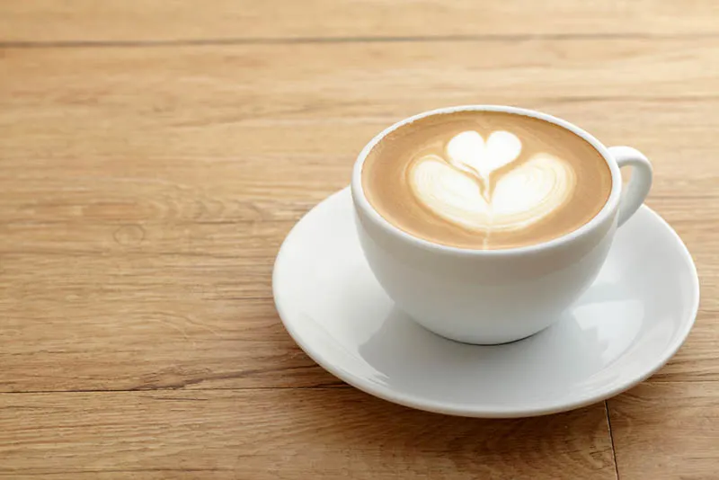 Eine Tasse Kaffee mit Herz-Muster in einer weißen Tasse auf Holztisch