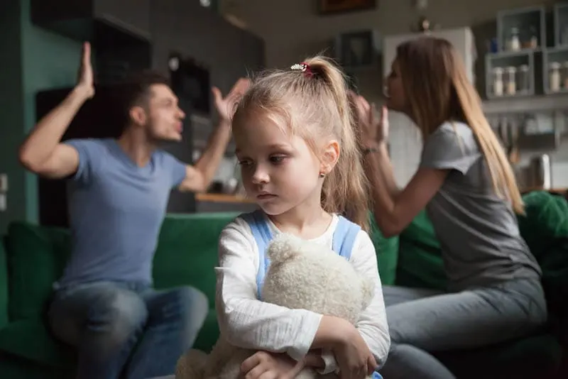 Eltern streiten sich, während trauriges kleines Mädchen ihren Teddybär umarmt