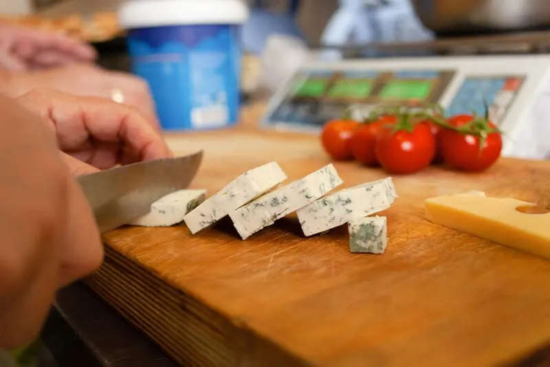 Frau schneidet Gorgonzola-Käse auf dem hölzernen Schneidebrett