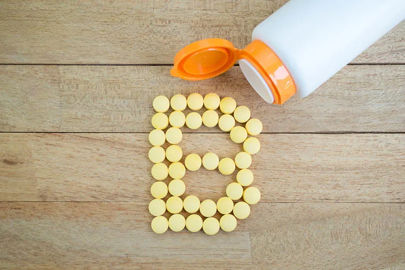 Gelbe Pillen, die auf einem Holztisch die Form des Alphabets B bilden