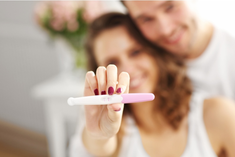 Glückliches Paar mit Schwangerschaftstest im Schlafzimmer