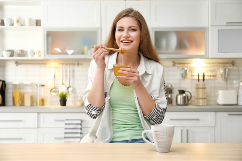 Positive junge Frau mit Honig in der Küche