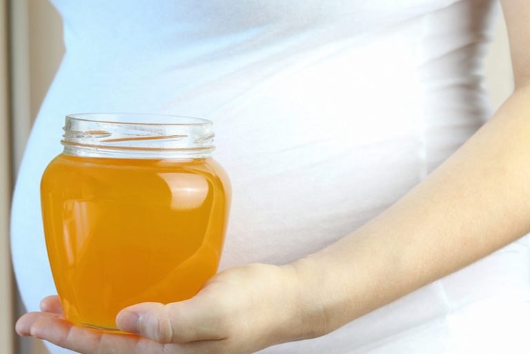 Glas mit Honig, Hand und Bauch einer schwangeren Frau