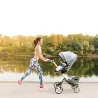 junge Mutter joggt mit Baby im Kinderwagen neben dem Fluss im Freien