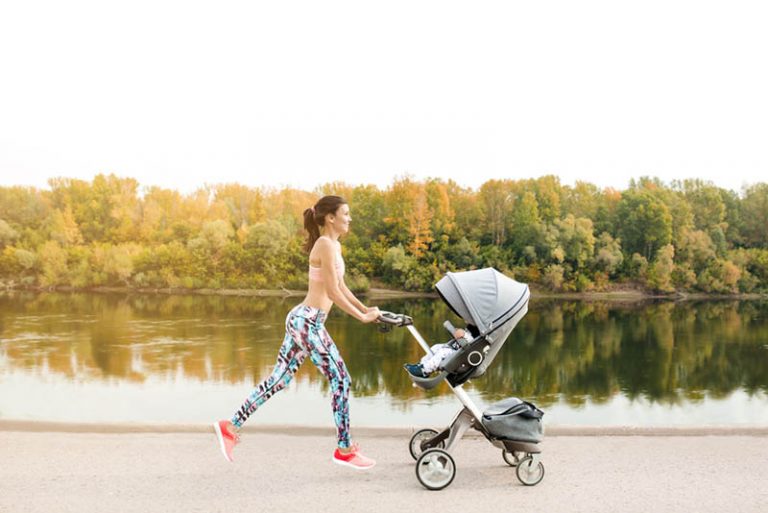 junge Mutter joggt mit Baby im Kinderwagen neben dem Fluss im Freien