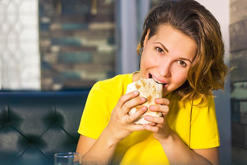 Junge Frau mit gelbem T-Shirt isst Kebab-Sandwich zu Hause