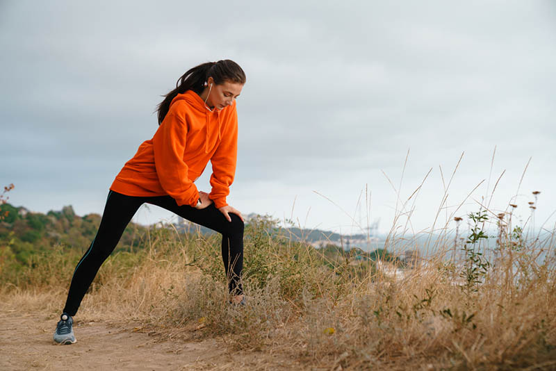 Junge Frau mit orangefarbenem Kapuzenpulli joggt im Freien