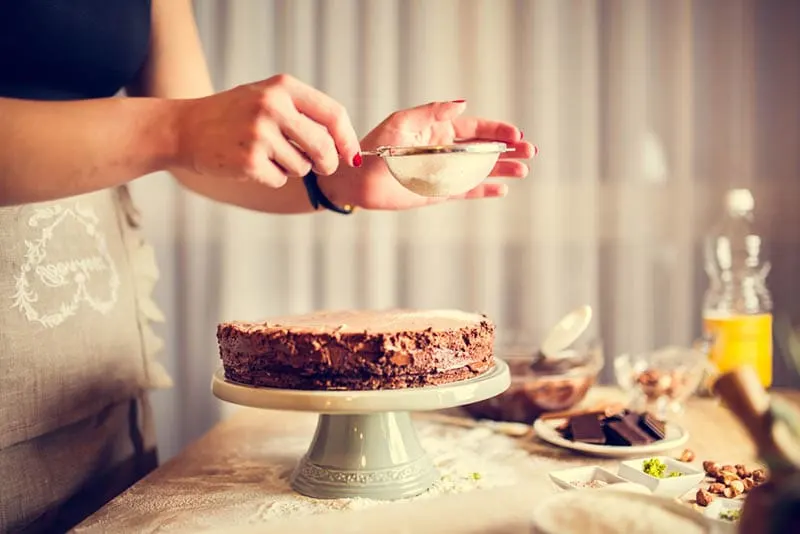 Junge Frau setzt Zucker auf Schokoladenkuchen auf dem Tisch