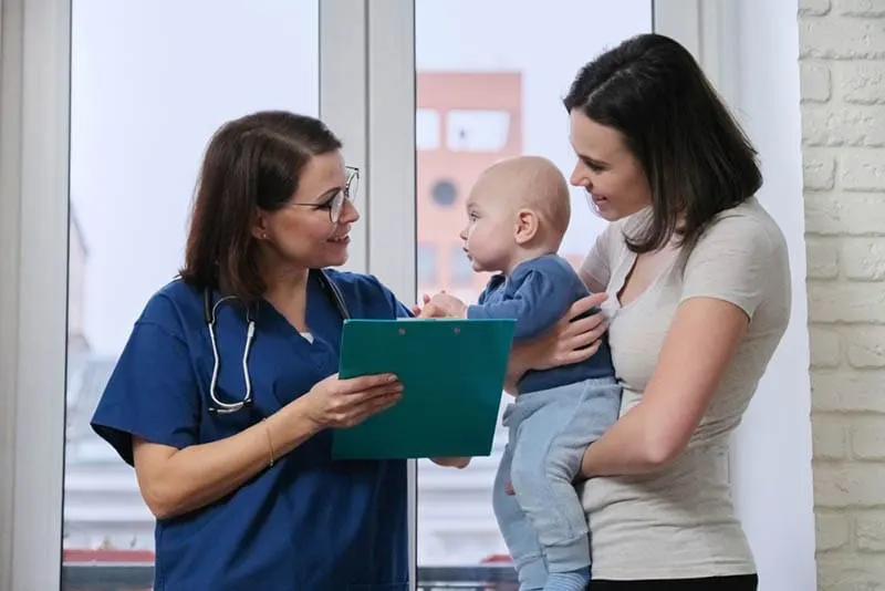 Junge Mutter hält ihr Baby im Gespräch mit dem Kinderarzt