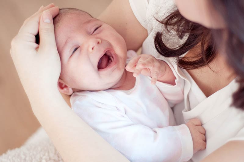 Junge Mutter hält weinendes Baby und überprüft seine Stirn