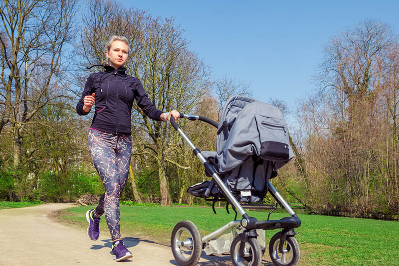 Junge Mutter joggt mit Baby im Kinderwagen im Park