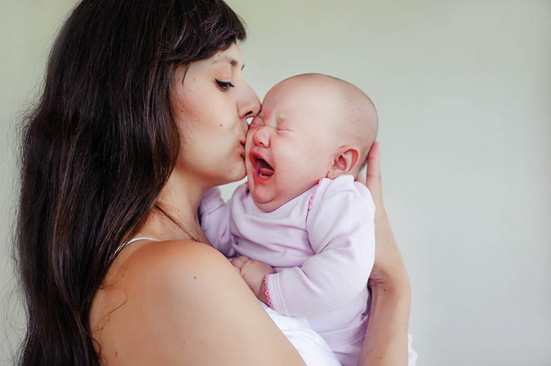Junge Mutter küsst weinendes Baby und versucht es zu beruhigen