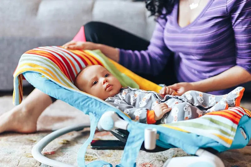 Junge Mutter sitzt auf dem Boden mit Baby in der Babywippe