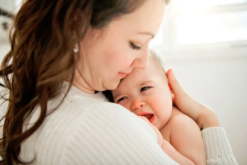 Junge Mutter tröstet ihr weinendes Baby in den Armen auf der Brust